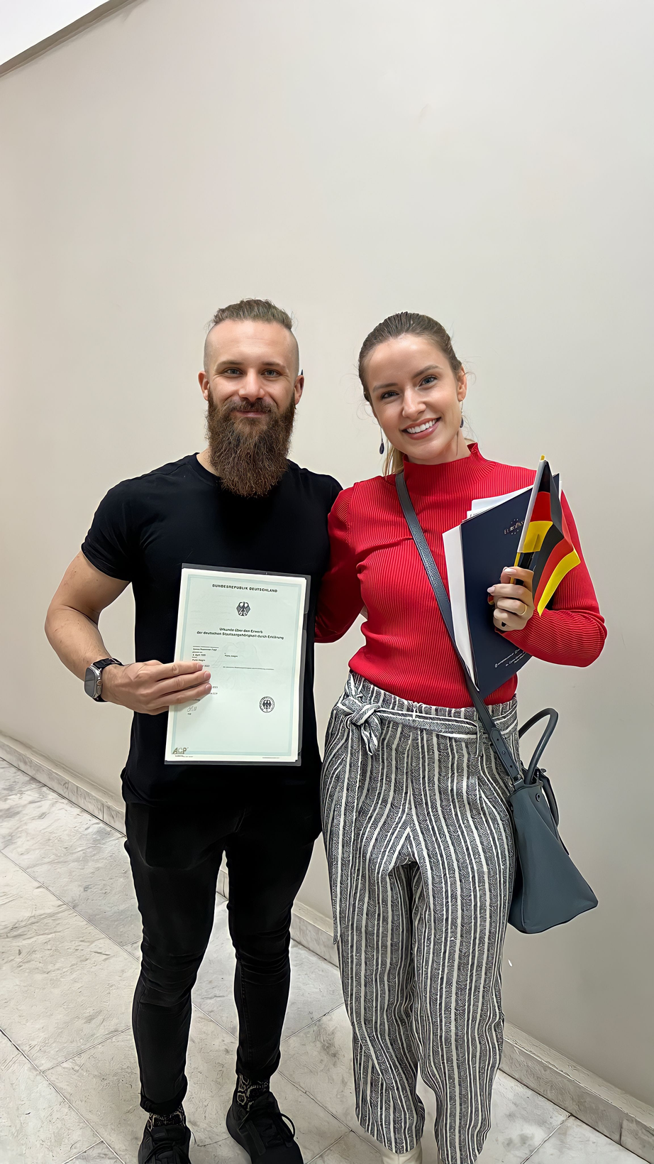 Casal sorrindo com o Certificado de Cidadania Alemã e a Pasta Europass em mãos
